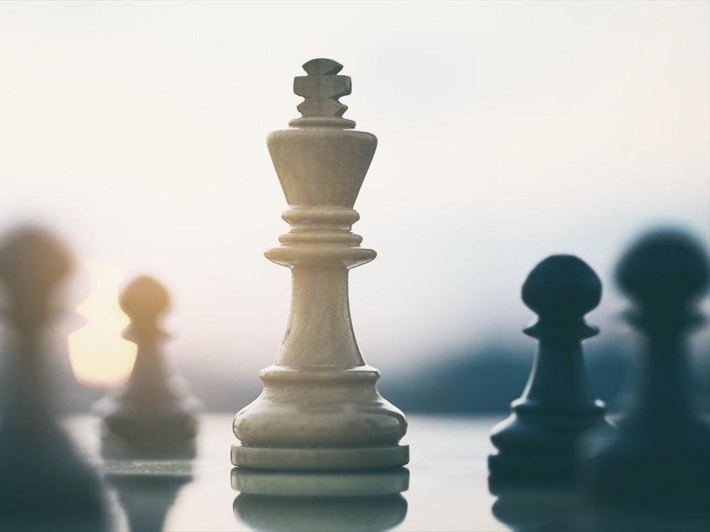 A chess king standing in front of the surrounding pieces on a board.